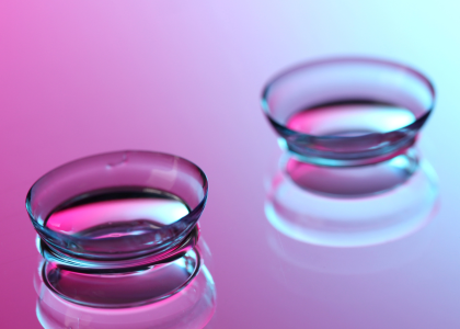 Two clear contact lenses are placed on a reflective surface with a pink and blue gradient background, showcasing both comfort and style for those seeking quality contacts in Coeur d’Alene.