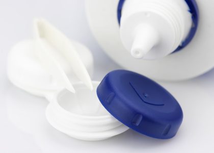 A white bottle of contact lens cleaner with a blue lid next to it.