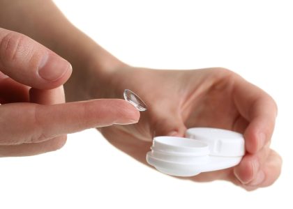 A person holding a contact lens with care on a white background.