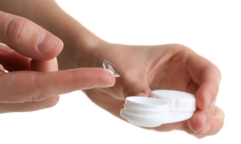 A person holding a contact lens with care on a white background.