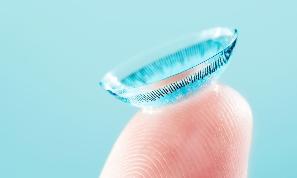 A person's finger with a small soft contact lens on it.