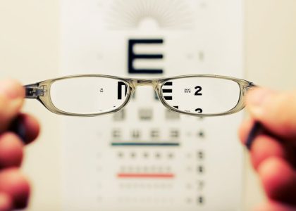 A person holding a pair of glasses in front of an eye chart to determine their eyeglass prescription.