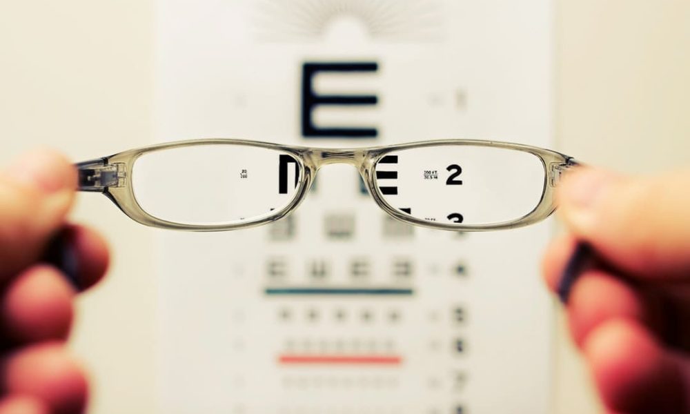 A person holding a pair of glasses in front of an eye chart to determine their eyeglass prescription.