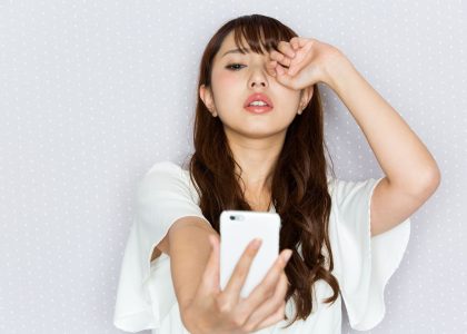A young asian woman taking a selfie with her phone, one eye slightly blurry.