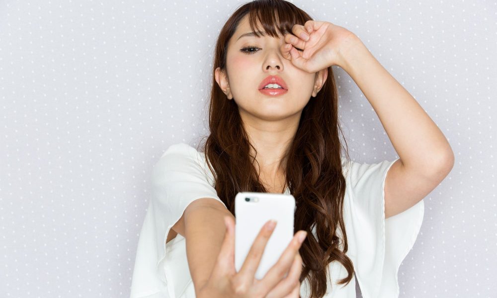 A young asian woman taking a selfie with her phone, one eye slightly blurry.